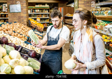 Employé de magasin d'aider jeune femme client de légumes choisissez dans le supermarché Banque D'Images