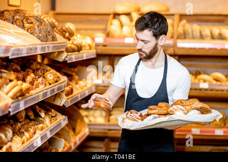 Beau Baker en uniforme mettant des pâtisseries sur les étagères dans le supermarché Banque D'Images