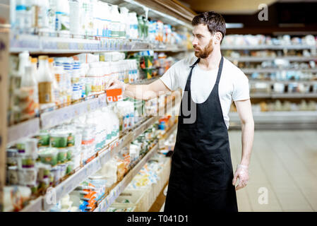 Employé de magasin à la recherche sur les bouteilles de lait, debout près de l'étagère avec les produits laitiers dans les supermarchés Banque D'Images