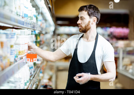 Employé de magasin à la recherche sur les bouteilles de lait, debout près de l'étagère avec les produits laitiers dans les supermarchés Banque D'Images