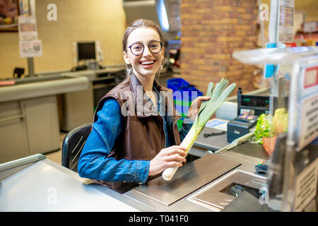 Portrait d'une femme heureuse et gaie comme caissier, assis à la caisse au supermarché Banque D'Images