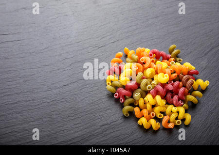 Pâtes spirales multicolores éparpillées sur un fond d'ardoise noire pour le texte de l'espace. Banque D'Images