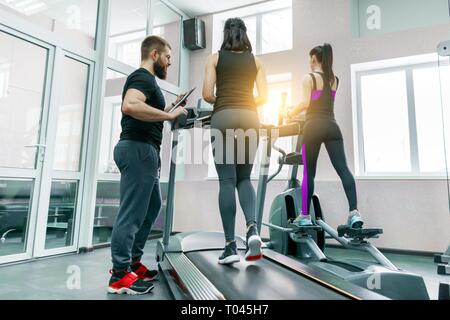 Les jeunes femmes athlétiques sur tapis roulant, instructeur personnel coaching et aider la femme du client. Fitness, le sport, la formation, les gens concept Banque D'Images