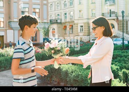 Fils adolescent a félicité mère surprise avec bouquet de fleurs, ville historique. Banque D'Images