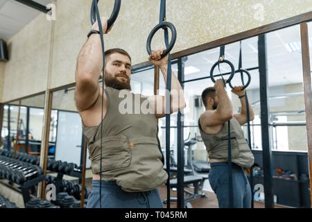 Homme barbu caucasien musclé faisant des exercices vêtus de gilet pondéré dans la salle de sport, style militaire. Banque D'Images