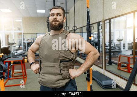 Portrait Portrait musculaire homme barbu habillé en veste pondéré dans la salle de sport, style militaire. Banque D'Images