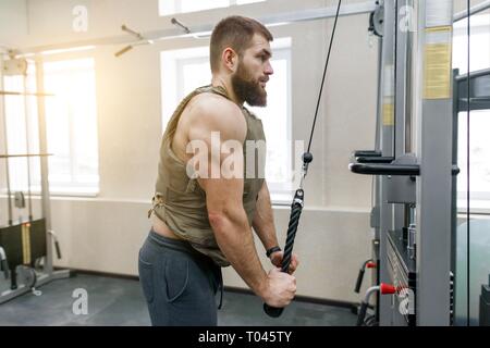 Homme barbu caucasien musclé faisant des exercices vêtus de gilet pondéré dans la salle de sport, style militaire. Banque D'Images