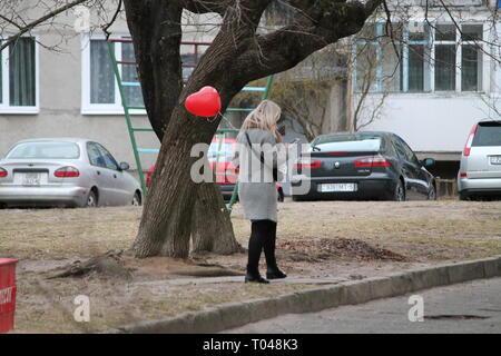 Fille blonde avec ballon rouge en forme de cœur à pied sur Spring Street Banque D'Images