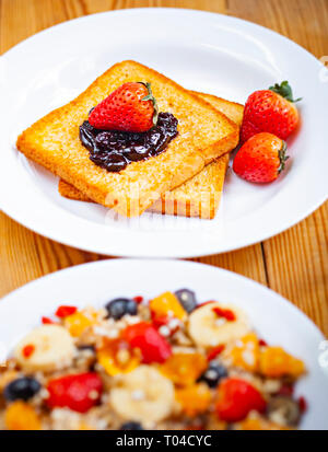 Table top image de pain grillé avec la confiture de canneberges de garnitures, fraise et mélange sain d'avoine fruits en plaque blanche sur table à manger en bois. Banque D'Images