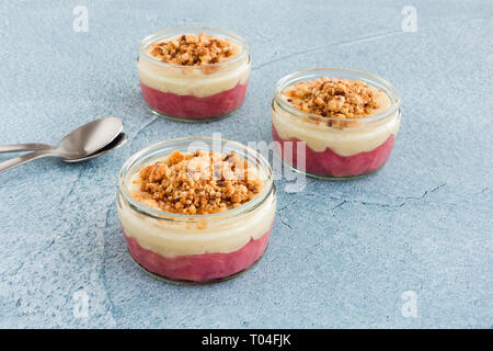 Libre de la rhubarbe et crème vanille malgache dessert avec des miettes en ce qui concerne le ciment de verre bleu fond avec copie espace. Banque D'Images
