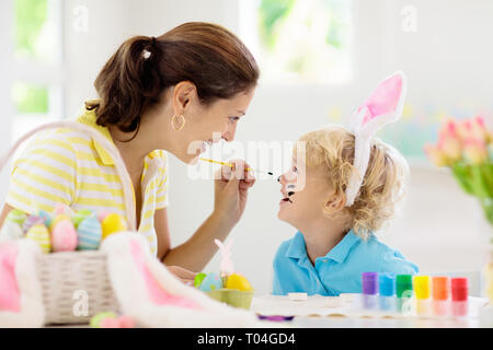 Mère et enfants la couleur des oeufs de Pâques. La peinture du visage pour petit enfant. Petit garçon aux oreilles de lapin et oeufs colorant mère. Chasse aux œufs de Pâques. Une célébration de la famille Banque D'Images