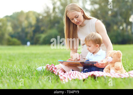 Mère avec enfant lit sur l'herbe dans le parc. Banque D'Images