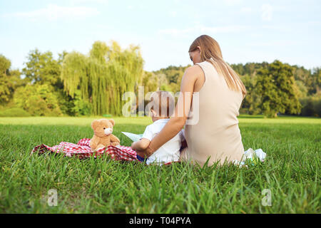 Mère avec enfant lit sur l'herbe dans le parc. Banque D'Images