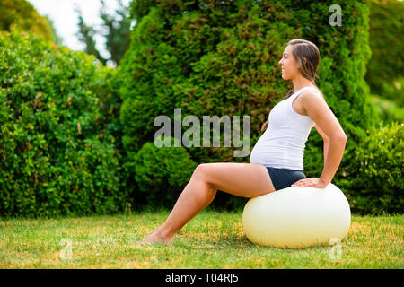 Pregnant Woman Sitting on Yoga Ball In Park Banque D'Images