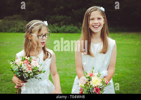 Beautiful happy smiling child et tween ou teen girl demoiselles en robes blanches holding hand-tied bouquets de saison dans un parc Banque D'Images