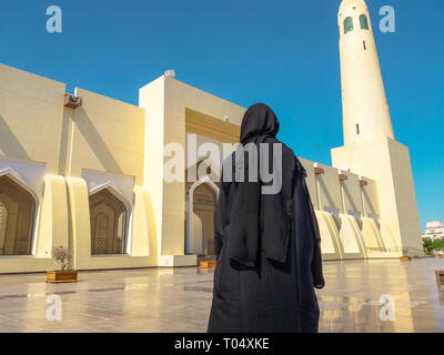 Dos de femme avec abaya robe à la façade et haut minaret de la Grande Mosquée de l'État à Doha, au Qatar, au Moyen-Orient, dans la péninsule arabique. Journée ensoleillée Banque D'Images