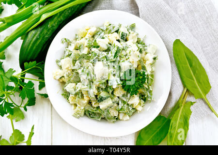 Salade de concombre, oseille, pommes de terre bouillies, les oeufs et les herbes, habillé avec de la mayonnaise dans une assiette blanche, le persil, les oignons verts et une serviette contre le ta Banque D'Images