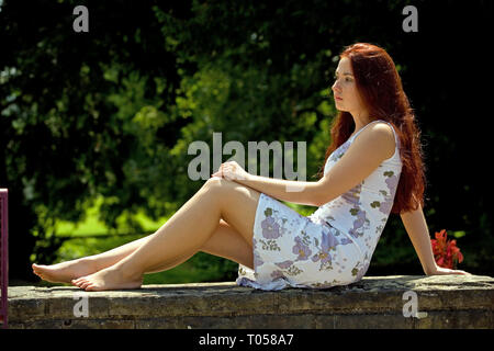 Une jeune femme est assise sur un mur de pierre et jouit du beau temps Banque D'Images