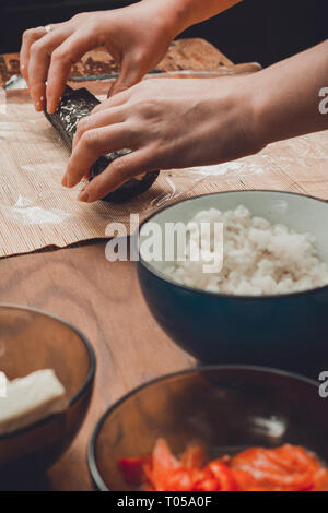 Une femme cuisinière prépare des sushis dans la cuisine et l'enveloppe d'une lettre à l'algue nori dans le rouleau 2019 Banque D'Images