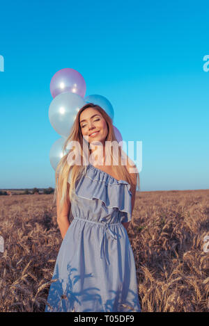 Belle et jeune fille se tient dans l'été dans un champ de blé. Dans sa main des ballons de couleur. Les émotions de joie et de plaisir sourire calme. Pensées de fantasy Banque D'Images