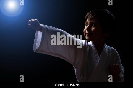 Karaté mignon garçon en kimono blanc isolé sur fond sombre. Enfant prêt pour les arts martiaux lutte. La lutte contre la formation de judo pour enfants. Meilleur concept pour marti Banque D'Images
