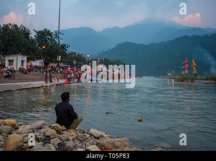 Un homme adulte seul assis sur les rochers au bord de la rivière dans une soirée. Personne n'est à l'opposé de l'appareil photo et souffre de dépression. Il n'y a Banque D'Images