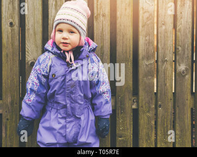 Little girl wearing purple coverall debout près de la barrière en bois Banque D'Images