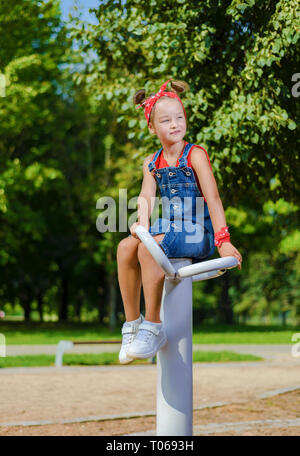 Jolie petite fille en denim et global capeline rouge et T-shirt jouant sur l'aire de jeux Banque D'Images