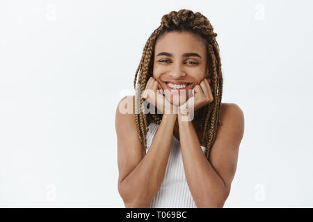 Tourné à l'intérieur de l'insouciance heureuse petite amie à la peau sombre avec des dreadlocks et renforts de tête penchée avec joie sourire sur palms contemplant avec admiration et Banque D'Images