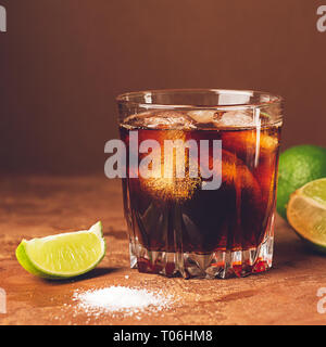 Verre à cocktail froid avec de la glace et des morceaux de citron vert juteux dans un verre sur un fond brun foncé. Close-up. Focus sélectif. Banque D'Images