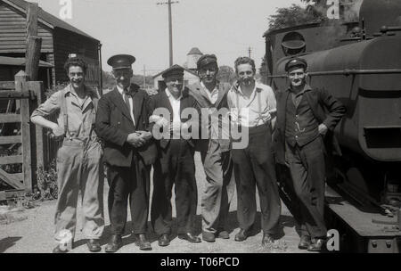 Années 1950, photo de groupe d'un chemin de fer de gare, des cheminots, conducteur de train et de former le personnel debout sur une plate-forme par une locomotive à vapeur, England, UK. Banque D'Images