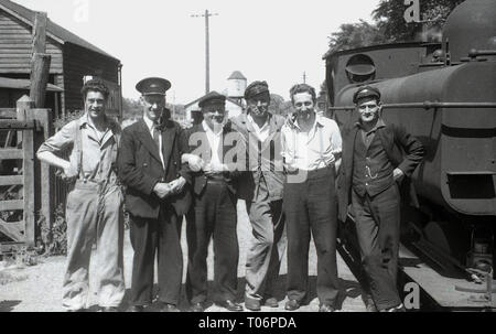 Années 1950, photo de groupe d'un chemin de fer de gare, des cheminots, conducteur de train et de former le personnel debout sur une plate-forme par une locomotive à vapeur, England, UK. Banque D'Images