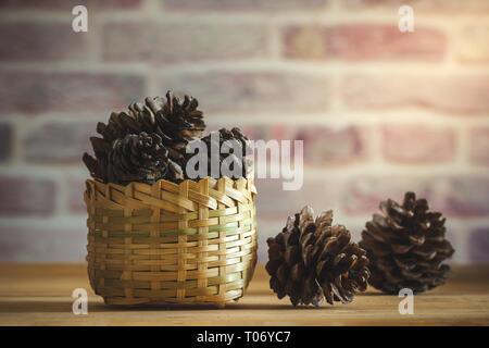 Cône de pin dans panier de bambou sur table en bois et mur de fond avec la lumière du soleil du matin. Banque D'Images