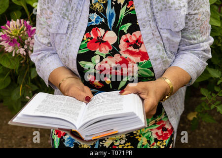 Plus femme juive de porter des bijoux lit son livre de prières dans le jardin. Réserver et mains close-up. Banque D'Images