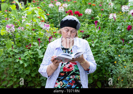 Plus femme juive de porter des bijoux lit son livre de prières dans le jardin. Banque D'Images