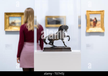 18 mars 2019, Bavaria, Munich : le modèle 'bronze' Cheval Turc par Antoine-Louis Barye (ca. 1835/1840) peut être vu dans l'exposition "Nature comme de l'Art - Paysage au 19e siècle, dans la peinture et la photographie' dans la Städtische Galerie in Lenbachhaus, tandis qu'une femme est à la recherche de peintures dans l'arrière-plan. Les œuvres des collections de la Fondation Christoph Heilmann et le Musée de la ville de Munich sera à l'exposition à partir de 19.03. à 18.08.2019. Photo : Matthias Balk/dpa Banque D'Images