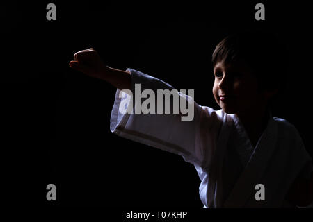 Karate boy en kimono blanc posant sur fond sombre. Enfant prêt pour les arts martiaux lutte. Lutte contre l'enfant à l'aïkido. Le mieux pour les combats martiaux et Banque D'Images