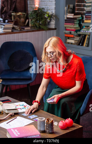 Aux cheveux blonds astrologue sentiment occupé lors de la lecture de cartes oracle Banque D'Images