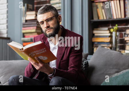 Homme sérieux sentiment lors de la lecture de livre sur l'astrologie d'argent Banque D'Images