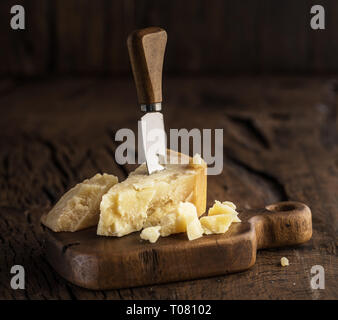 Morceau de fromage Parmesan et de couteau sur la planche de bois. Fond sombre. Banque D'Images