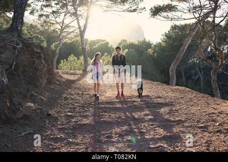 Teenage boy and girl hiking avec chien noir en bois au coucher du soleil Banque D'Images