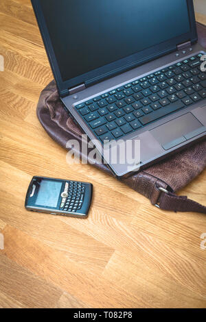 Un ordinateur portable avec une sacoche en cuir, sur une table en bois à côté d'un téléphone mobile. Banque D'Images