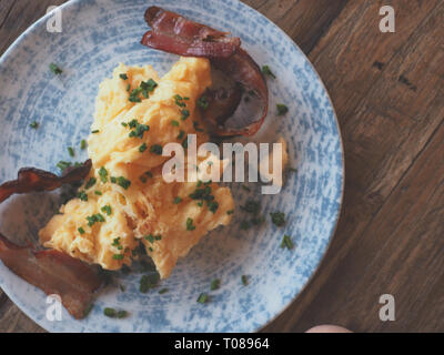 De délicieux œufs brouillés avec du bacon et la ciboulette sur une table en bois rustique, tsty concept de petit-déjeuner, vue d'en haut Banque D'Images