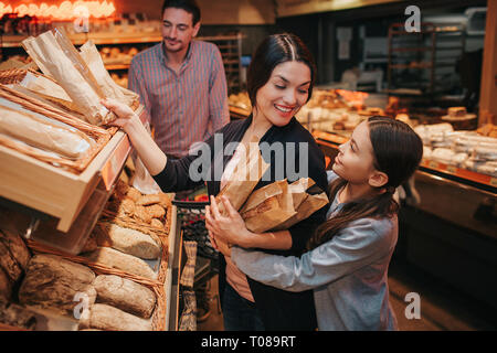 Les jeunes parents et fille en épicerie. Mère fille gaie et choisissez l'UPB Pain et petits pains ensemble. Ils sourient à l'autre. Homme debout derrière Banque D'Images