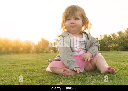 Funny little girl sitting on grass en vacances Banque D'Images