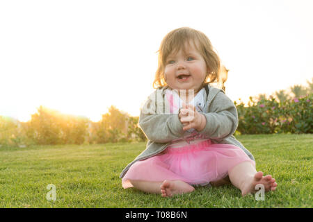 Peu drôle baby girl sitting on the grass Banque D'Images