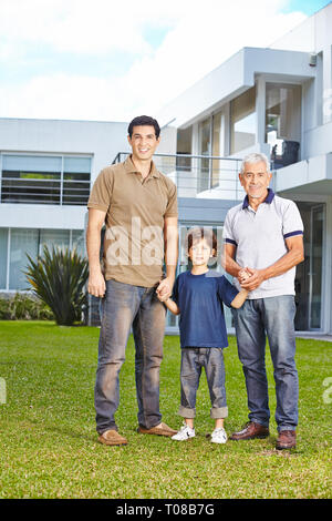 Heureux l'enfant est debout avec un père et un grand-père devant la maison dans le jardin Banque D'Images