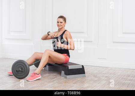 Heureux belle jeune femme caucase athlétique shorts rose et noir top emplacement, boire de l'eau et se reposer après une intervention sur le sport. Piscine, s Banque D'Images