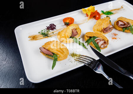 Mousse au fromage avec du bacon dans eclair, servi sur une assiette et couverts de vert et de tomate cherry Banque D'Images