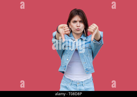 Portrait d'insatisfaits belle brune jeune femme avec le maquillage permanent style décontracté denim, pouce vers le bas et à la recherche à l'appareil photo avec l'aversion. en Banque D'Images